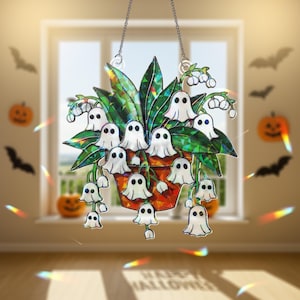 Può includere: Un acchiappasole a tema Halloween con un vaso di foglie verdi stilizzate e figure di fantasmi bianchi. Il vaso è di colore rosso-arancio. L'acchiappasole è appeso a una catena. Lo sfondo include zucche, pipistrelli e il testo "HAPPY HALLOWEEN".