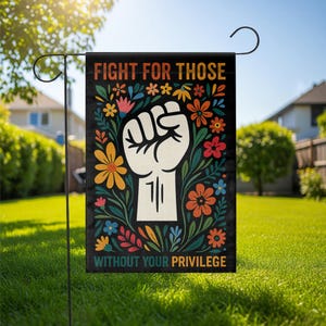 May include: A black garden flag with the text "FIGHT FOR THOSE WITHOUT YOUR PRIVILEGE" in orange and white. The flag features a white fist and colorful flowers. The flag is displayed in a grassy garden.
