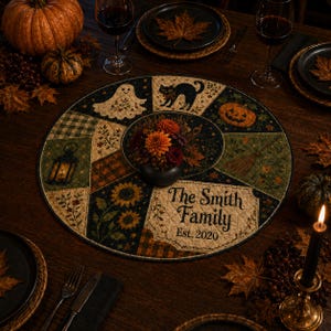 May include: A round quilted fabric table mat featuring a patchwork design with Halloween motifs including a ghost, black cat, jack-o'-lantern, lantern, and sunflowers. The text reads The Smith Family Est. 2020. A small dark bowl with flowers sits in the center.