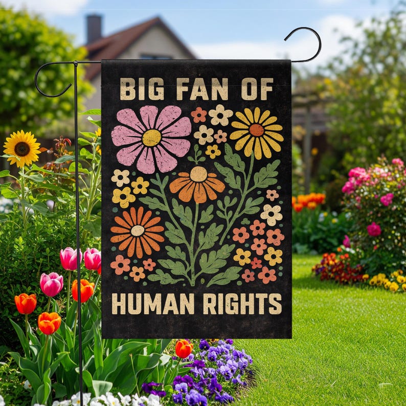 May include: A rectangular black garden flag featuring the text BIG FAN OF HUMAN RIGHTS in a bold, light-colored font. The design includes a central illustration of various stylized flowers in shades of pink, yellow, and orange with green leaves.