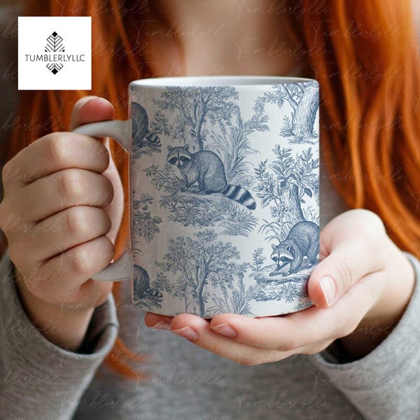 Może przedstawiać: Biały kubek ceramiczny z niebiesko-białym wzorem z szopami i drzewami. Kubek jest trzymany przez dłonie osoby.