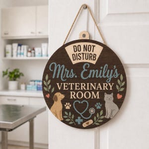 May include: A circular dark wood sign hanging by a rope with the text DO NOT DISTURB Mrs. Emily's VETERINARY ROOM. The sign features a tan dog, a gray cat, a blue stethoscope, paw prints, a medical cross, a bandage, and green leaf accents.