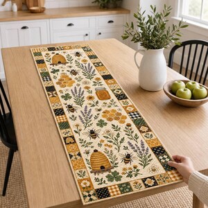 Könnte beinhalten: Ein rechteckiger Tischläufer mit cremefarbener Mitte und einem wiederkehrenden Muster aus Honigbienen, Bienenstöcken, Waben, Lavendelzweigen und Klee. Der Rand besteht aus einem Patchwork-Design in den Farben Gelb, Grün und Schwarz.