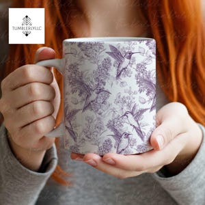 Puede incluir: Taza de cerámica blanca con un patrón de colibríes y flores moradas.