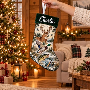 May include: A Christmas stocking with a dark green velvet cuff featuring the name Charlie in white script. The body displays a nature scene with a deer, a mallard duck, a fish, and a fishing rod against a snowy forest and lake background.