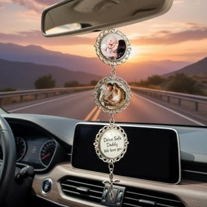 May include: A car charm with three decorative, silver-colored, circular pendants. The top two pendants feature framed photos. The bottom pendant has the text "Drive Safe Daddy We love you". The charm hangs from the rearview mirror.