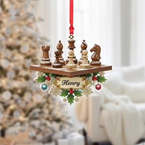 May include: A Christmas ornament featuring a chess set on a wooden board. The ornament includes a red ribbon for hanging, a decorative border with holly, berries, and snowflakes, and the name "Henry" in elegant script.