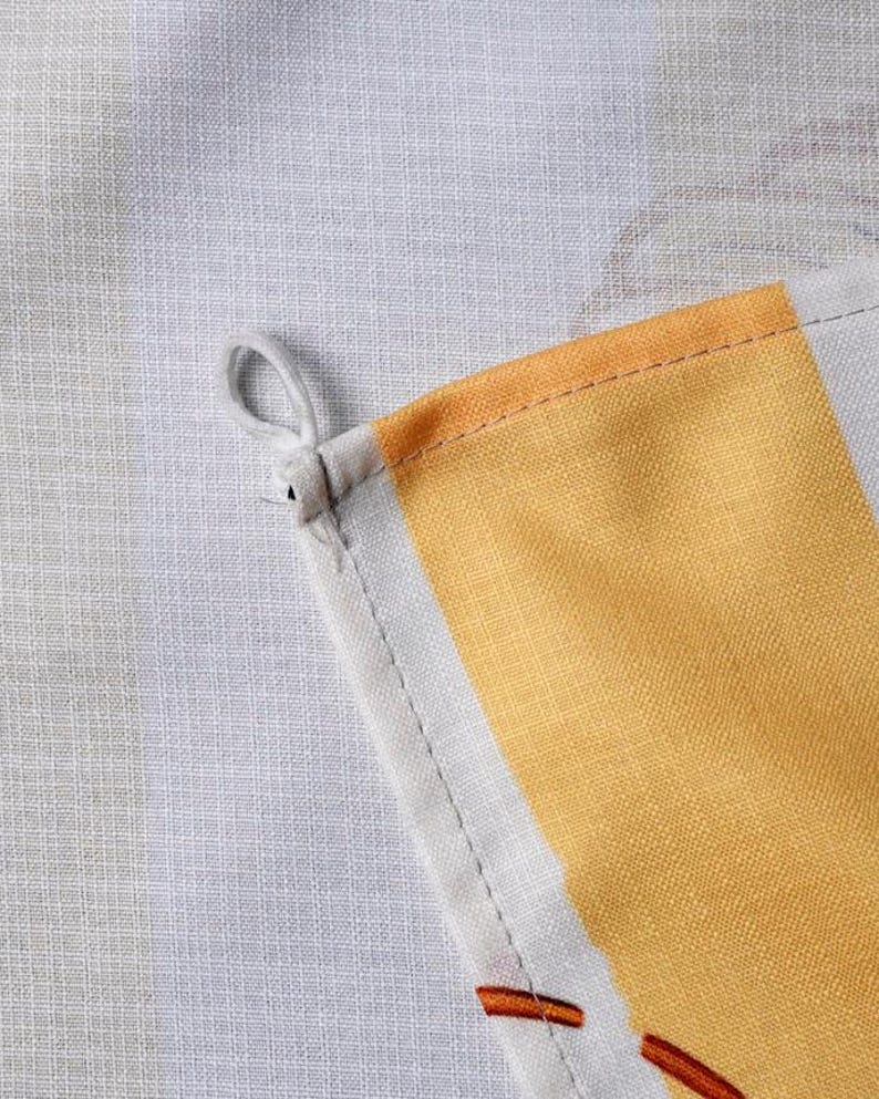Puede incluir: Un pa&ntilde;o de cocina de tela tejida con un patr&oacute;n de cuadros blancos y gris claro con una prominente franja vertical amarilla. La esquina del pa&ntilde;o incluye un peque&ntilde;o lazo de tela blanca para colgar, con costuras visibles a lo largo del dobladillo.