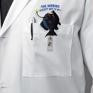 May include: A white lab coat with a black anglerfish badge that says "The Horrors Persist But So Do I".