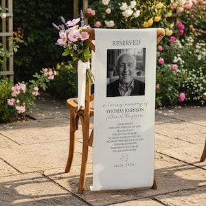 Puede incluir: Un letrero conmemorativo de tela blanca sobre una silla de madera, con un retrato en blanco y negro de Thomas Johnson, el texto RESERVED, in loving memory of THOMAS JOHNSON, father of the groom, un poema y la fecha 10.10.2026.