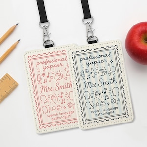Puede incluir: Dos cordones para tarjetas de identificación con el texto "professional yapper" y "Mrs. Smith" en una fuente caprichosa. Una insignia es de color rosa claro, la otra azul marino. Ambas tienen gráficos relacionados con el habla y el título "logopeda".