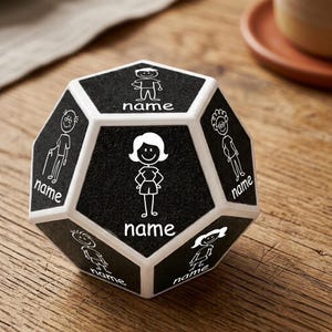 May include: A black and white dodecahedron-shaped family keepsake. Each of the twelve faces features a stick figure illustration and the word "name" below it. The faces are black with white borders and illustrations.