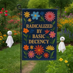 Op de afbeelding: Een marineblauwe tuinvaandel met kleurrijke bloemmotieven en de gouden tekst "RADICALIZED BY BASIC DECENCY". Twee kleine, witte spookachtige figuren staan aan weerszijden van de vlag, in een tuin.