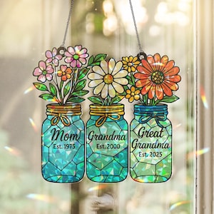 May include: A stained glass suncatcher featuring three teal mason jars with flowers. The jars are labeled Mom Est. 1975, Grandma Est. 2000, and Great Grandma Est. 2025. The design includes pink, white, and orange flowers with green leaves.