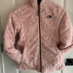 May include: A pink fleece jacket with a black zipper and the North Face logo on the left chest.