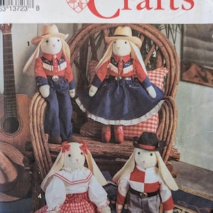 Puede incluir: Un patrón de costura Simplicity Crafts para hacer cuatro muñecas de conejo. El patrón incluye instrucciones para hacer una muñeca de conejo vaquero, una muñeca de conejo vaquera, una muñeca de conejo con un vestido de cuadros rojos y blancos y una muñeca de conejo con una camisa a cuadros rojos y negros y pantalones vaqueros. El número del patrón es 8270.
