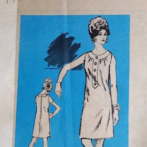May include: Vintage sewing pattern for a sleeveless dress with a button-up front. The pattern is printed on a blue background and features a black and white illustration of a woman wearing the dress. The pattern is labeled "Lawrence Gross Printed Pattern Prominent Designer M217 - SIZE 12".