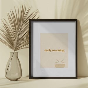 May include: A black framed print with a beige background and the text "early morning" in gold lettering. A stylized sun graphic is below the text.
