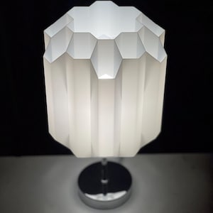 May include: A white table lamp with a geometric, pleated shade and a chrome base.