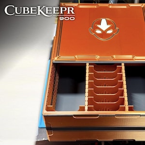 Peut inclure: Une boîte de rangement CubeKeeper 900 de couleur cuivre avec un couvercle ouvert. Le couvercle présente un emblème doré. L'intérieur comporte plusieurs compartiments pour organiser les objets. La boîte est conçue avec une esthétique géométrique détaillée.