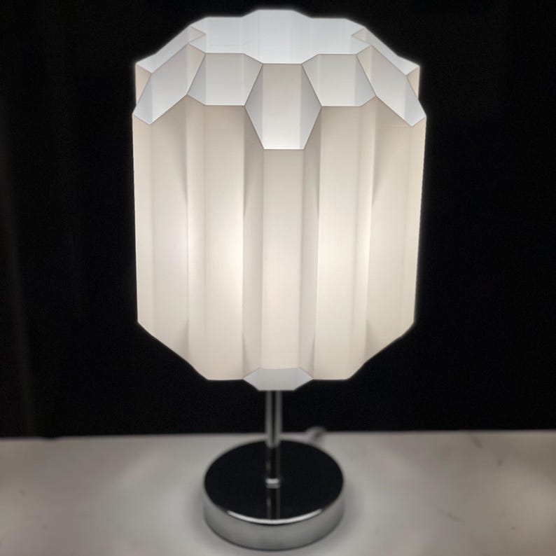 May include: A white table lamp with a geometric, pleated lampshade and a chrome base.