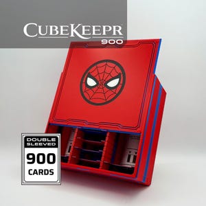 Puede incluir: Una caja de almacenamiento de tarjetas CubeKeepr 900 roja y azul con un gráfico de telaraña negra y ojos blancos en la tapa. El interior contiene divisores azules e insertos blancos. Una etiqueta lateral muestra el texto Double Sleeved 900 Cards.