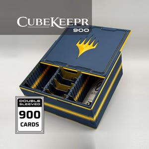 May include: A navy blue card storage box labeled CubeKeepr 900 with a yellow flame logo on the lid. The interior features yellow dividers and slots for cards. A white rectangular graphic on the side displays the text Double Sleeved 900 Cards.