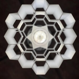 Op de afbeelding: Witte plafondlamp met een honingraatontwerp. De lamp is gemaakt van wit metaal en heeft een ronde vorm.