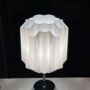 Op de afbeelding: Een witte tafellamp met een geometrische, gefacetteerde kap en een chromen voet.