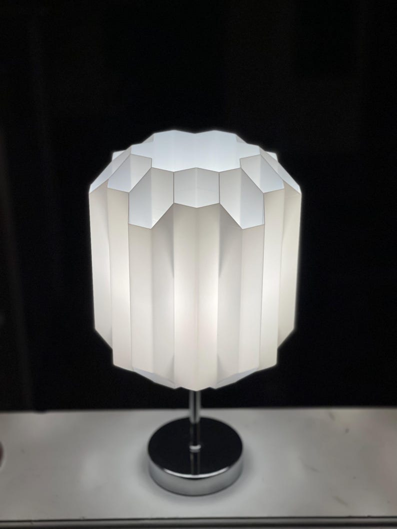 Op de afbeelding: Een witte tafellamp met een geometrische, gefacetteerde kap en een chromen voet.