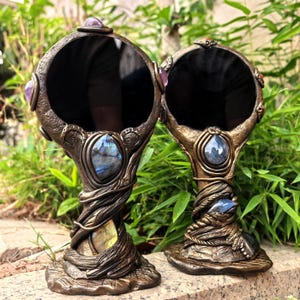 Puede incluir: Dos espejos de mano redondos con marcos texturizados de color bronce que presentan detalles esculpidos en forma de enredadera. Cada espejo está adornado con piedras preciosas pulidas incrustadas, incluyendo labradorita iridiscente y amatista morada.