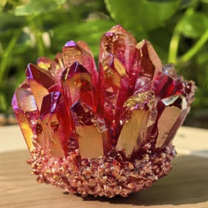 Op de afbeelding: Een cluster van levendige, rood-oranje kristallen met iriserende paarse en gouden punten. De kristallen zijn gegroepeerd, waardoor een getextureerde, opvallende weergave ontstaat. De basis van de cluster heeft een ruwe, korrelige textuur.