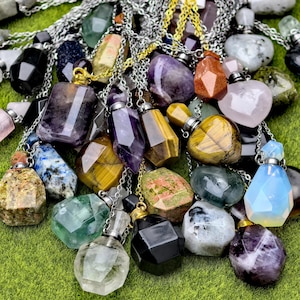 May include: A collection of gemstone pendant necklaces in various shapes and colors, including amethyst, tiger's eye, and clear quartz. Each pendant is attached to a silver chain. The pendants are displayed on a green surface.