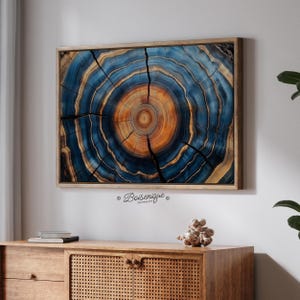 May include: A framed wood slice art piece with a detailed cross-section design. The artwork features concentric rings in shades of blue, brown, and orange, with natural cracks. The piece is mounted in a wooden frame and hangs above a wooden cabinet.