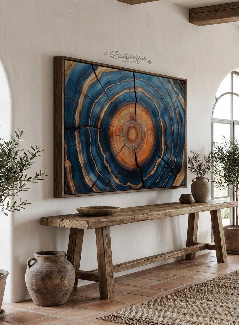 May include: Large framed artwork featuring a cross-section of a tree trunk, showcasing concentric rings in shades of blue and orange. The artwork is displayed above a rustic wooden console table, creating a natural and earthy aesthetic.