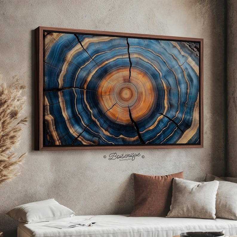 May include: A framed wall art print featuring a cross-section of a tree trunk. The artwork showcases concentric rings in shades of blue, orange, and brown, with visible cracks. The frame is a dark brown color. The artwork is signed "Boiserique".