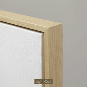 May include: Close-up of a canvas art piece with a light oak wood frame. The canvas is white and stretched tightly within the frame. The frame is a light, natural wood color. The text "Light Oak" is at the bottom.