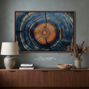 May include: A framed wood slice art piece with concentric rings in shades of blue and orange. The artwork is displayed on a teal wall above a wooden cabinet. The piece is from Boisenique.