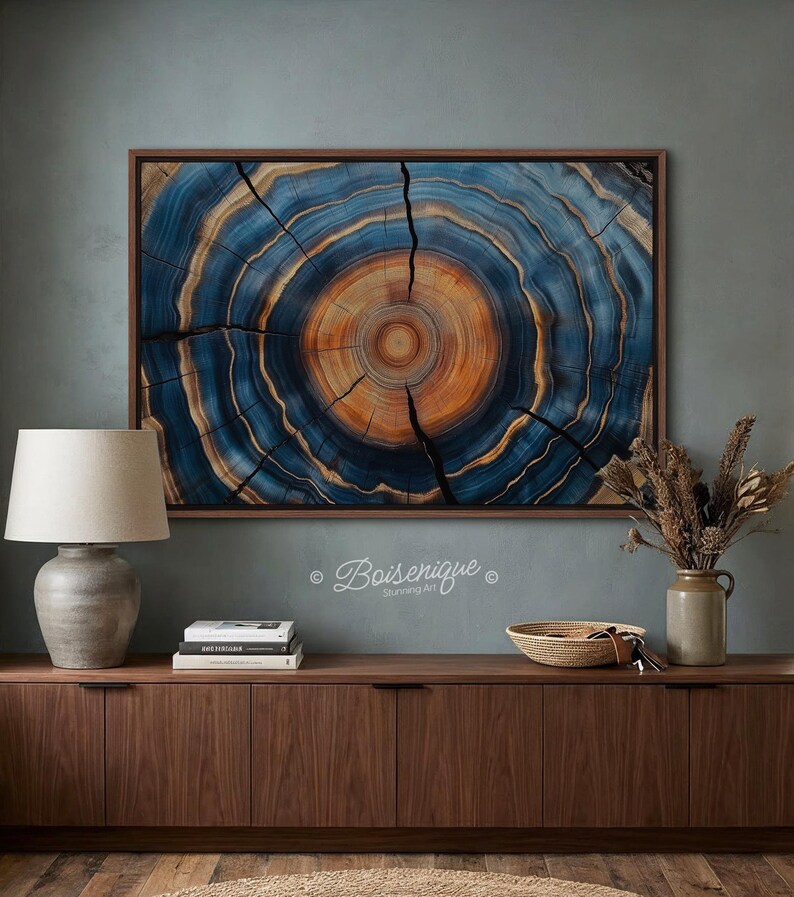 May include: A framed wood slice art piece with concentric rings in shades of blue and orange. The artwork is displayed on a teal wall above a wooden cabinet. The piece is from Boisenique.