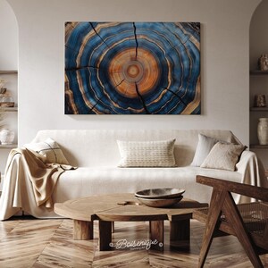 May include: A large, rectangular wall art piece depicting a cross-section of a tree trunk. The artwork features concentric rings in shades of blue, brown, and gold. The piece is mounted above a cream-colored sofa in a living room setting.