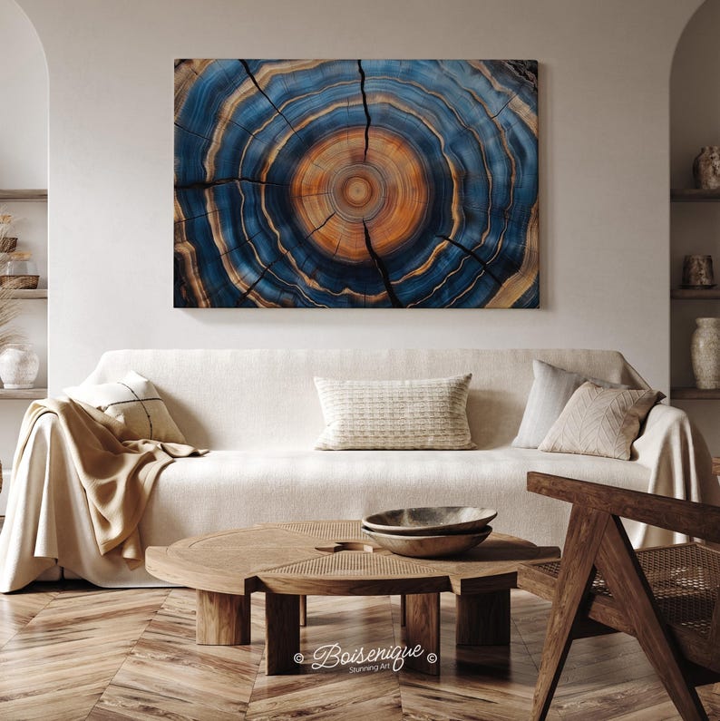 May include: A large, rectangular wall art piece depicting a cross-section of a tree trunk. The artwork features concentric rings in shades of blue, brown, and gold. The piece is mounted above a cream-colored sofa in a living room setting.