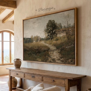 May include: A framed landscape painting depicting a path leading to a small house, with trees and a cloudy sky. The painting is in a wooden frame and hangs above a wooden console table. The room has a neutral color palette.