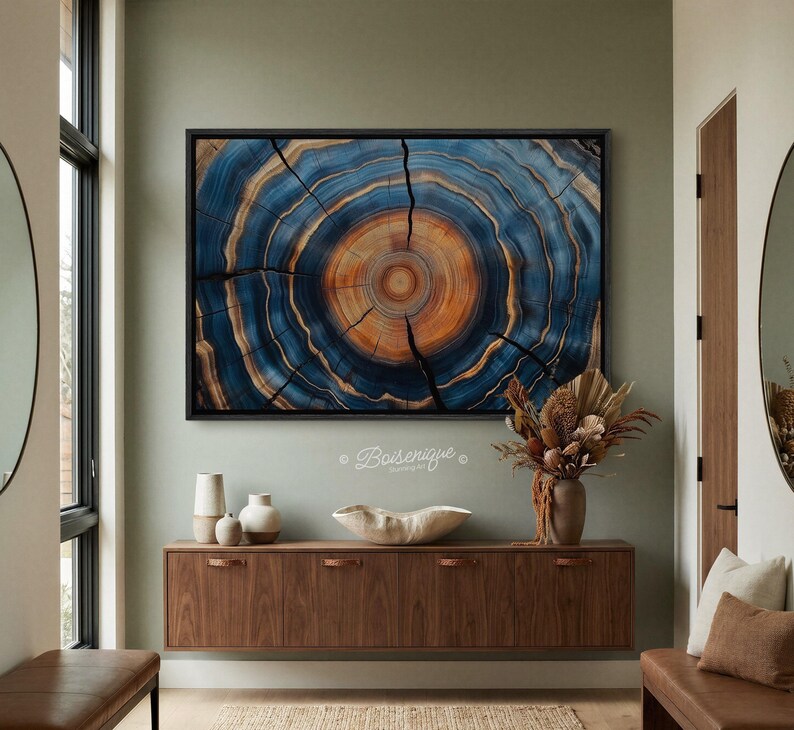 May include: A framed artwork featuring a close-up of a tree cross-section. The artwork displays concentric rings in shades of blue, brown, and orange, with visible cracks. The piece is mounted on a light green wall above a wooden cabinet.
