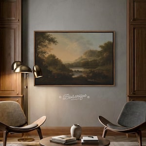 May include: A framed landscape painting of a lake scene with trees and mountains. The artwork is in a wooden frame and hangs on a grey wall. The room also features a floor lamp, chairs, and a coffee table.