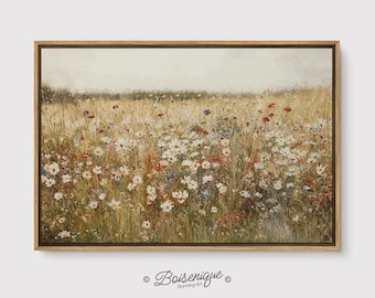 May include: A framed canvas print of a field of wildflowers in a meadow. The artwork features a variety of flowers in white, red, and blue, set against a backdrop of tall, golden grass. The frame is a light brown color. The artist's signature is in the bottom left corner.