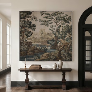 May include: A large framed tapestry depicting a landscape scene with trees, a river, and a distant building. Below, a dark wood console table holds books, vases, and a candle holder. The room has white walls and dark trim.