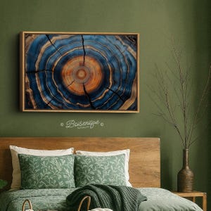 May include: A framed artwork featuring a cross-section of a tree trunk, showcasing concentric rings in shades of blue and orange. The artwork is displayed on a green wall above a bed with green pillows and a wooden headboard. The text "Boisenique" is visible.