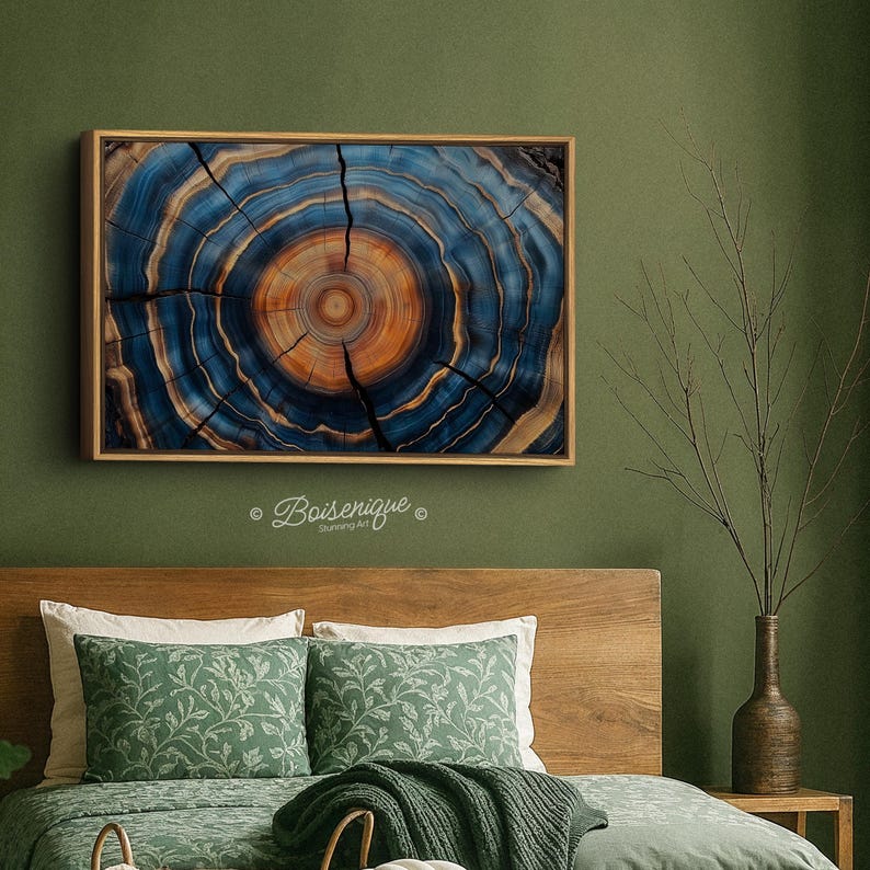May include: A framed artwork featuring a cross-section of a tree trunk, showcasing concentric rings in shades of blue and orange. The artwork is displayed on a green wall above a bed with green pillows and a wooden headboard. The text "Boisenique" is visible.