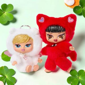 May include: Two Bratz baby dolls. One doll is in a white fuzzy bear costume with a silver keychain. The other doll is in a red fuzzy costume with heart-shaped ears. Both dolls have large eyes, full lips, and detailed makeup.