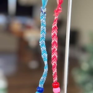 May include: Two friendship bracelets with beads. One bracelet is blue and white, the other is red and white.